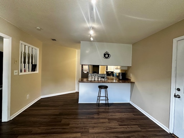 2761 Tyndall Dr, Valdosta, GA 31602 - kitchen with dark countertops, dark wood-style flooring, a peninsula, a kitchen breakfast bar, and a textured ceiling