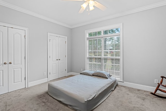 bedroom featuring light carpet, two closets, ceiling fan, and ornamental molding