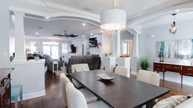 dining space with ornate columns, dark hardwood / wood-style flooring, ceiling fan with notable chandelier, and ornamental molding