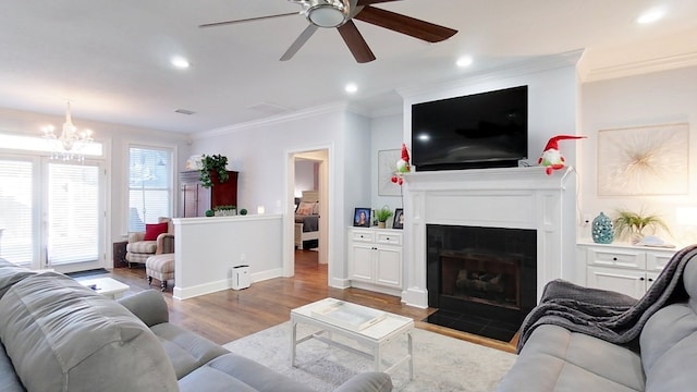 living room with a tile fireplace, light hardwood / wood-style floors, ceiling fan with notable chandelier, and ornamental molding