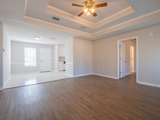 empty room with a tray ceiling, ceiling fan, wood-type flooring, and ornamental molding