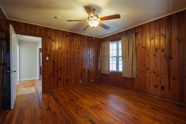 empty room featuring wooden walls, ceiling fan, dark wood-type flooring, and ornamental molding