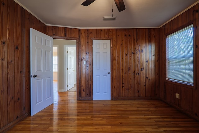 unfurnished bedroom with ceiling fan, wood-type flooring, wood walls, and ornamental molding