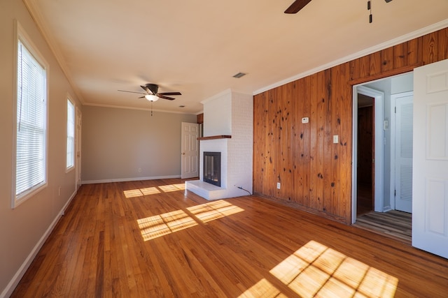 unfurnished living room with ornamental molding, ceiling fan, wood-type flooring, a fireplace, and wood walls