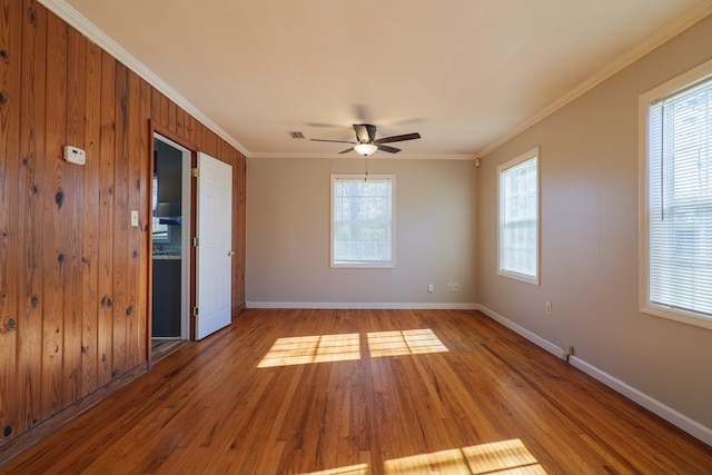 empty room featuring hardwood / wood-style flooring, ceiling fan, wood walls, and crown molding