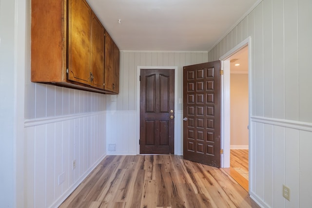 interior space featuring light wood-type flooring, ornamental molding, and wooden walls