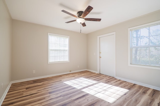 empty room featuring a wealth of natural light, crown molding, ceiling fan, and light wood-type flooring