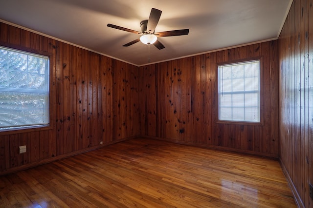 spare room with ceiling fan, a healthy amount of sunlight, wooden walls, and light hardwood / wood-style flooring