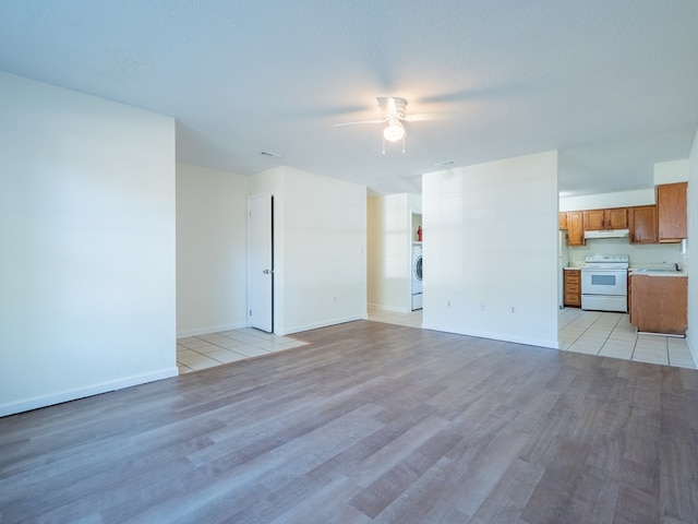 unfurnished living room featuring ceiling fan, washer / dryer, a textured ceiling, and light hardwood / wood-style flooring