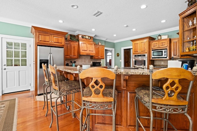 4155 Quail Run Cir, Valdosta, GA 31601 - kitchen featuring appliances with stainless steel finishes, backsplash, crown molding, brown cabinetry, and light stone countertops