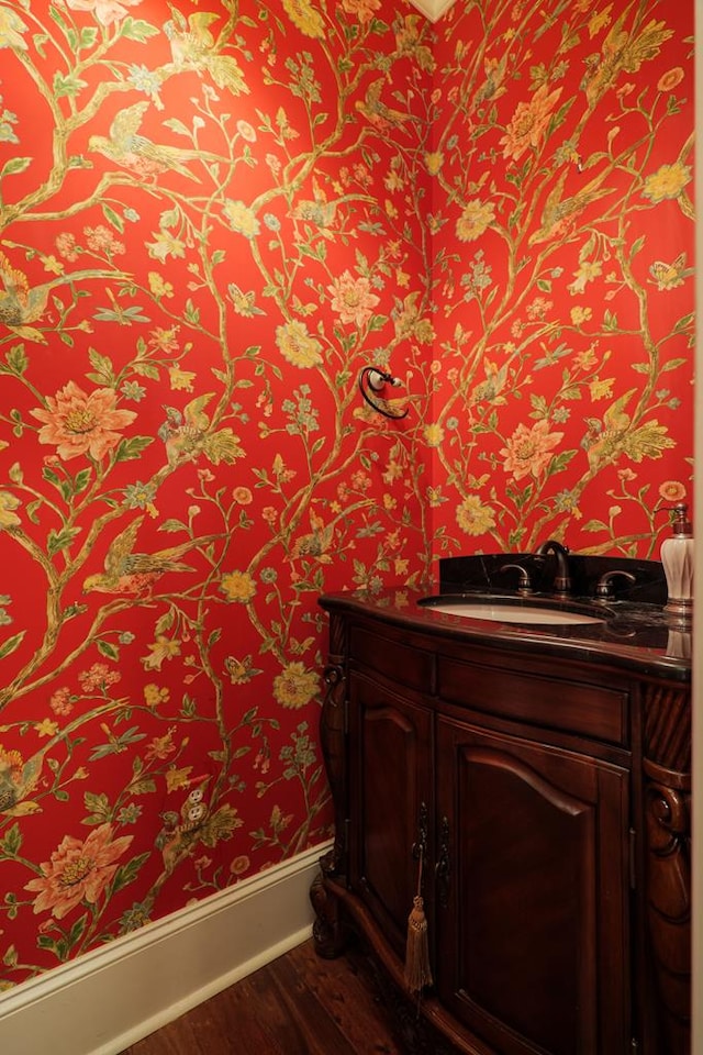 bathroom featuring baseboards, wood finished floors, vanity, and wallpapered walls