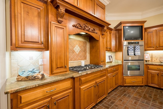kitchen with brick floor, appliances with stainless steel finishes, brown cabinetry, and crown molding