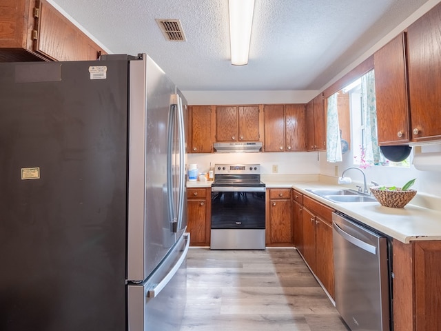 kitchen with stainless steel appliances, sink, a textured ceiling, and light hardwood / wood-style floors