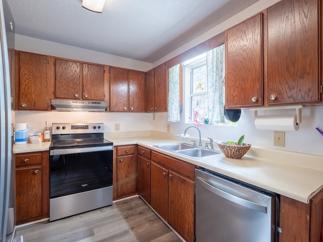 kitchen with stainless steel appliances, sink, a textured ceiling, and light wood-type flooring