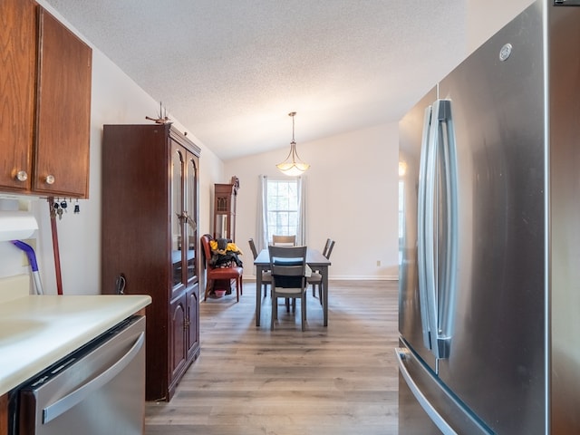 kitchen featuring vaulted ceiling, hanging light fixtures, light hardwood / wood-style floors, stainless steel appliances, and a textured ceiling