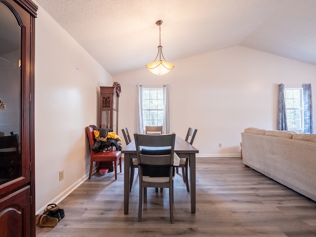 dining area featuring dark wood-type flooring, a textured ceiling, and vaulted ceiling