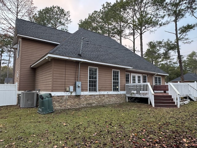 back house at dusk featuring central AC, a deck, and a lawn