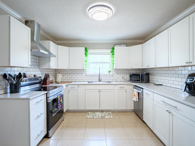 kitchen with appliances with stainless steel finishes, wall chimney range hood, sink, light tile patterned floors, and white cabinetry