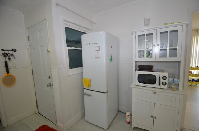 kitchen featuring white refrigerator, ornamental molding, and white cabinets