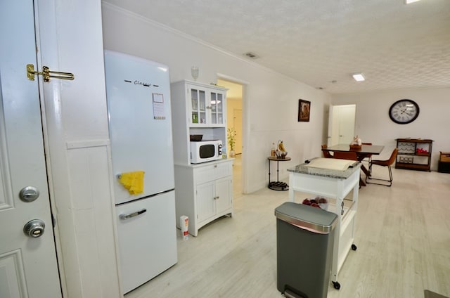 kitchen with white cabinetry, white appliances, light hardwood / wood-style floors, crown molding, and a textured ceiling