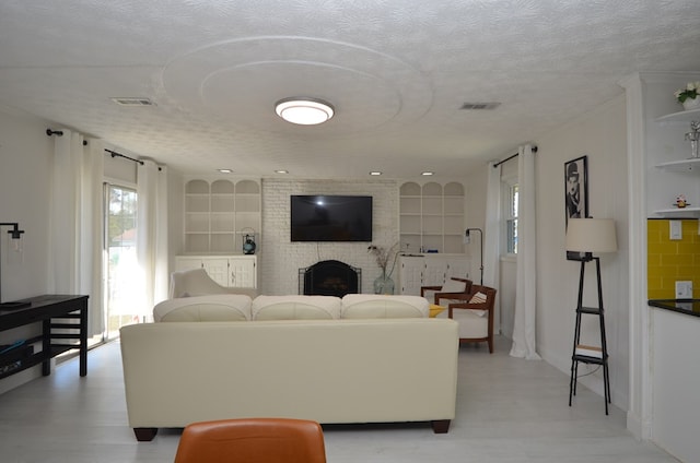 living room featuring a brick fireplace, built in features, and a textured ceiling