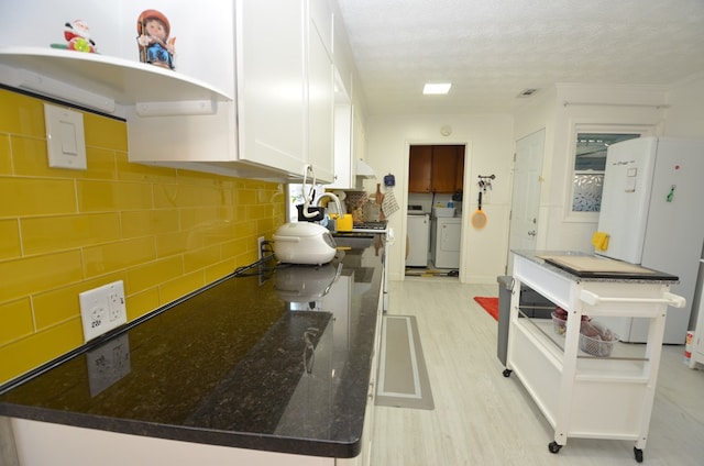 kitchen featuring separate washer and dryer, white cabinets, decorative backsplash, light hardwood / wood-style floors, and a textured ceiling