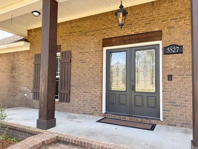 view of exterior entry with brick siding and a porch