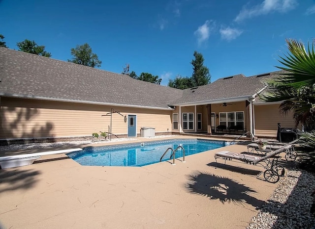 outdoor pool with ceiling fan, a diving board, and a patio