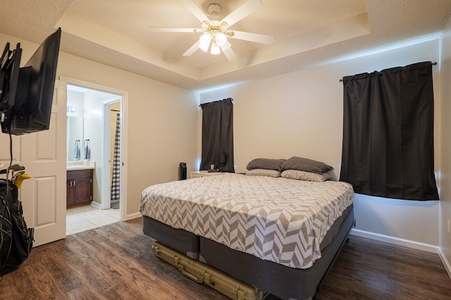 bedroom featuring a ceiling fan, a raised ceiling, ensuite bath, and wood finished floors