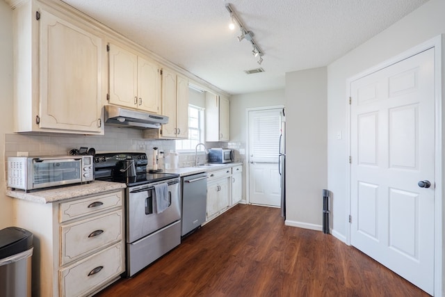 kitchen featuring track lighting, dark wood-type flooring, under cabinet range hood, backsplash, and stainless steel appliances