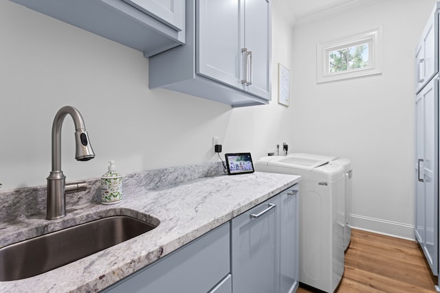 washroom with crown molding, a sink, light wood-style floors, cabinet space, and washing machine and dryer
