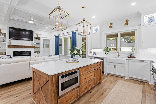 kitchen featuring white cabinets, stainless steel appliances, a glass covered fireplace, and a sink