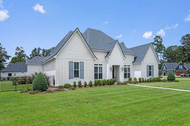 view of front of house with fence, board and batten siding, a shingled roof, and a front yard