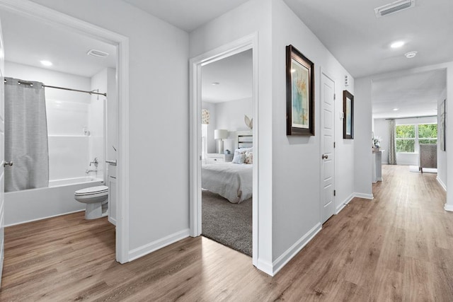 hall featuring wood finished floors, visible vents, and baseboards