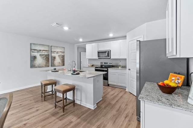 kitchen featuring a breakfast bar area, stainless steel appliances, a sink, white cabinets, and light wood finished floors