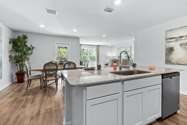 kitchen with light stone counters, visible vents, stainless steel dishwasher, a sink, and light wood-type flooring