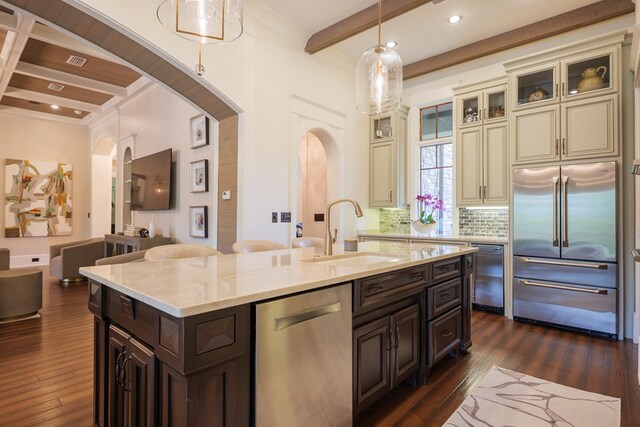 kitchen with dark brown cabinetry, sink, beamed ceiling, cream cabinets, and appliances with stainless steel finishes