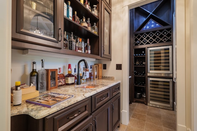 bar featuring dark brown cabinets, light stone counters, sink, and beverage cooler