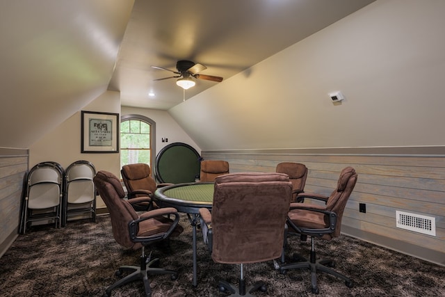 home office featuring wooden walls, ceiling fan, dark carpet, and vaulted ceiling