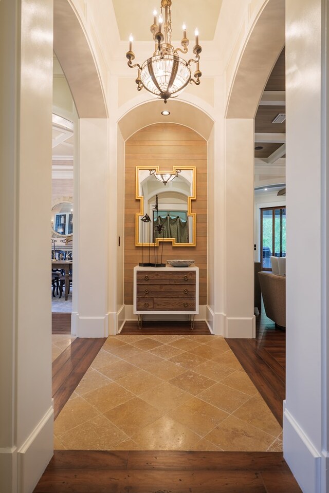 corridor featuring beamed ceiling, wood-type flooring, ornamental molding, and a notable chandelier