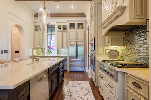 kitchen with appliances with stainless steel finishes, tasteful backsplash, custom exhaust hood, sink, and cream cabinets