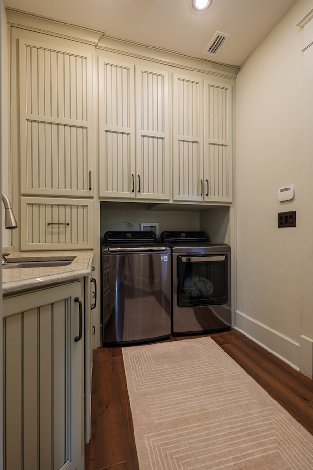 clothes washing area with dark hardwood / wood-style flooring, washer and dryer, sink, and cabinets