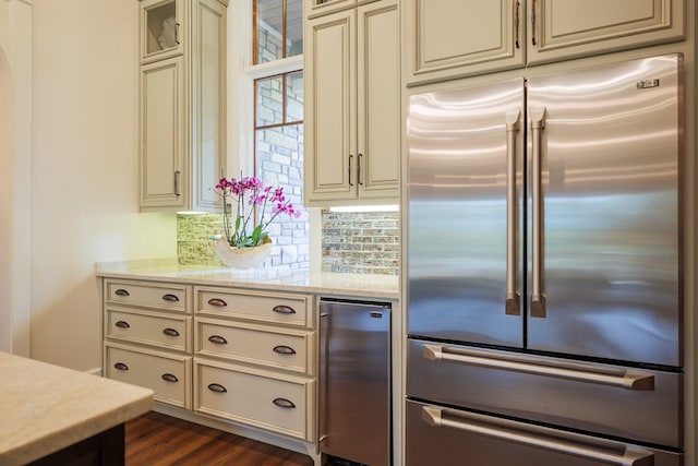 kitchen with decorative backsplash, high end refrigerator, light stone countertops, dark wood-type flooring, and cream cabinets