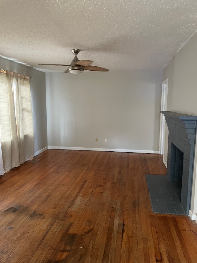 unfurnished living room featuring ceiling fan, dark hardwood / wood-style floors, a textured ceiling, and a brick fireplace