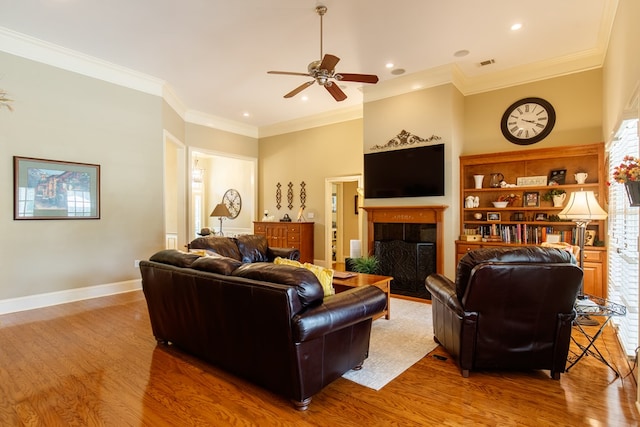 living room featuring visible vents, a tile fireplace, light wood finished floors, ornamental molding, and a ceiling fan