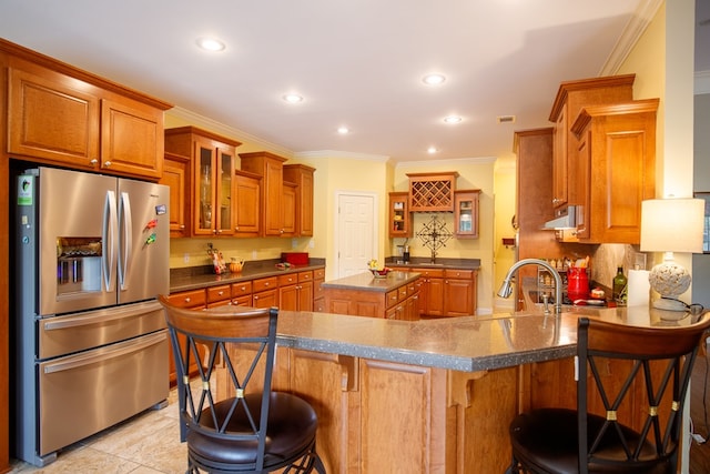 kitchen featuring a peninsula, brown cabinets, under cabinet range hood, stainless steel fridge with ice dispenser, and a kitchen breakfast bar