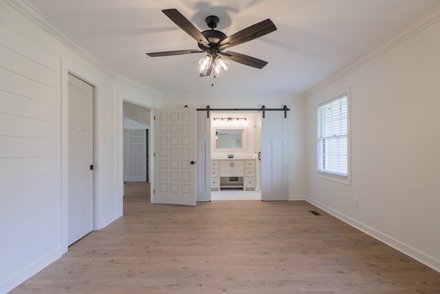 unfurnished bedroom with light wood-type flooring, ensuite bathroom, ceiling fan, crown molding, and a barn door