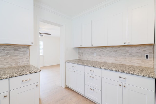 kitchen with white cabinets, light stone countertops, light wood-type flooring, and backsplash