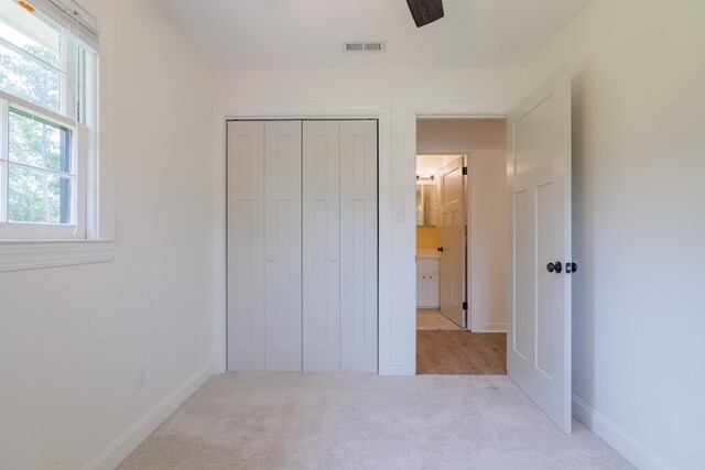 unfurnished bedroom with a closet, light colored carpet, and ceiling fan