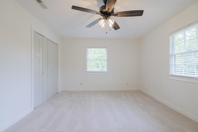 unfurnished bedroom with light colored carpet, multiple windows, and ceiling fan